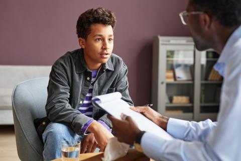 A teenage boy is sitting talking to a male counselor or therapist