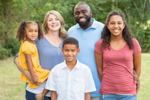 A diverse family poses together for a portrait outside, they're all smiling.